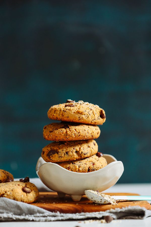 close up image of a stack of pantry staple trail mix cookies in a white bowl against a dark background