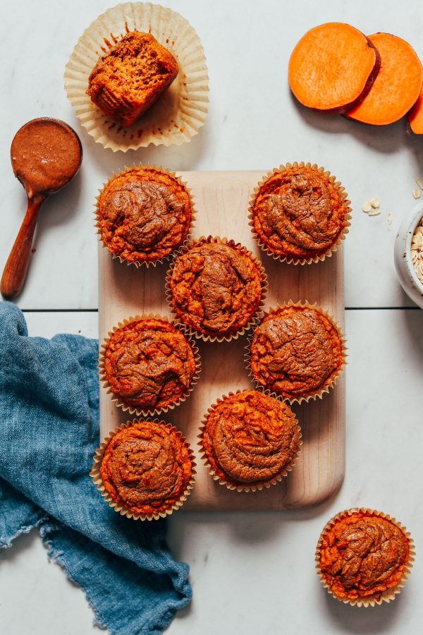 birds eye view of multiple almond butter sweet potato muffins for social isolation on a wooden surface next to sweet potato slices and a spoon of almond butter