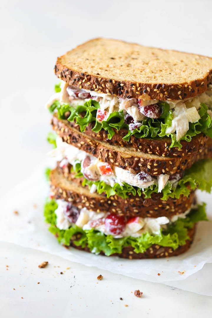 close up of two chicken salad sandwiches on brown bread stacked on top of one another on a white counter top