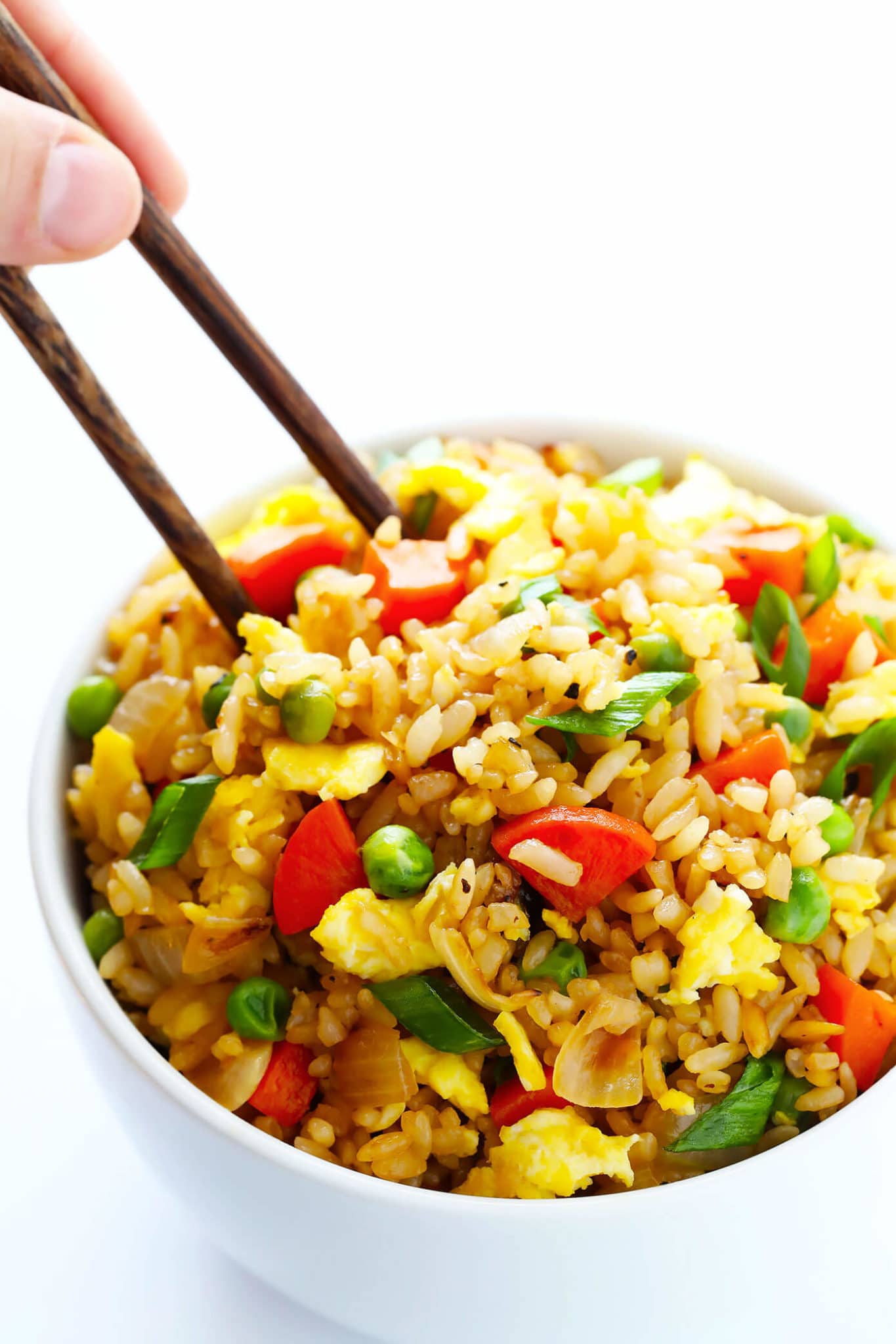 close up of pantry staple fried rice garnished with green onions served in a white bowl with brown chopsticks