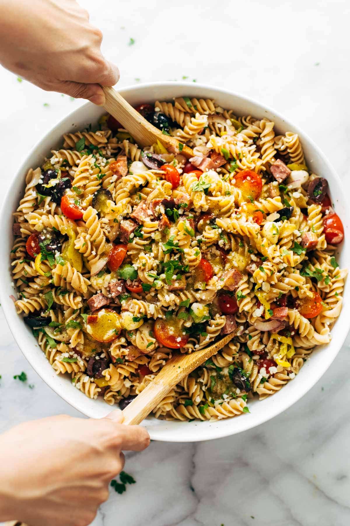 birds eye view of pantry staple quick and easy pasta salad served in a white bowl with wooden serving spoons