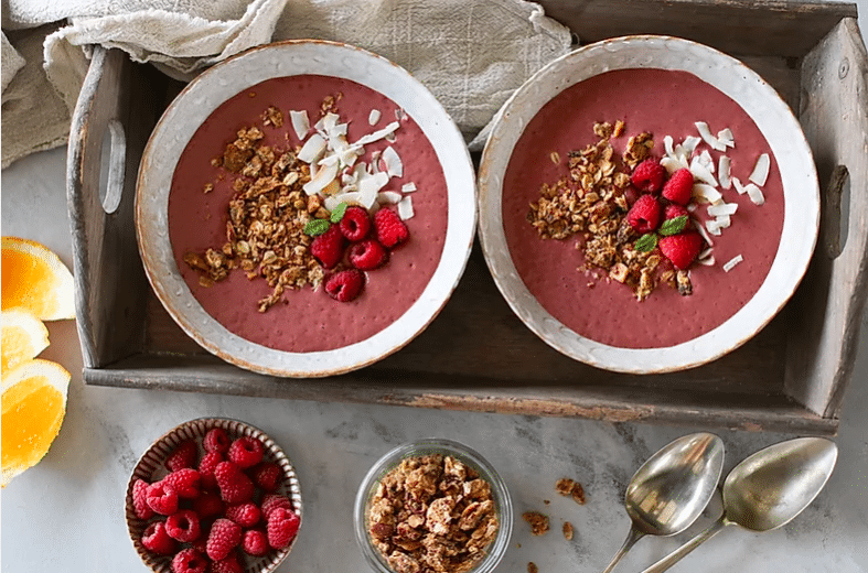 birds eye view of two immune booster smoothie bowls for social isolation garnished with granola and fruit next to two bowls filled with nuts and fruit