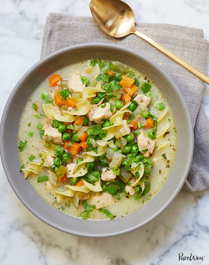 birds eye view of slow cooker chicken noodle soup in a grey bowl garnished with fresh herbs next to a rose gold spoon for social isolation