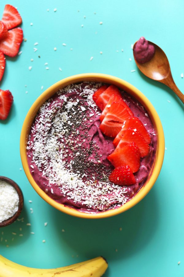 birds eye view of five minute smoothie bowl topped with seeds and fruit in a yellow bowl against a blue background