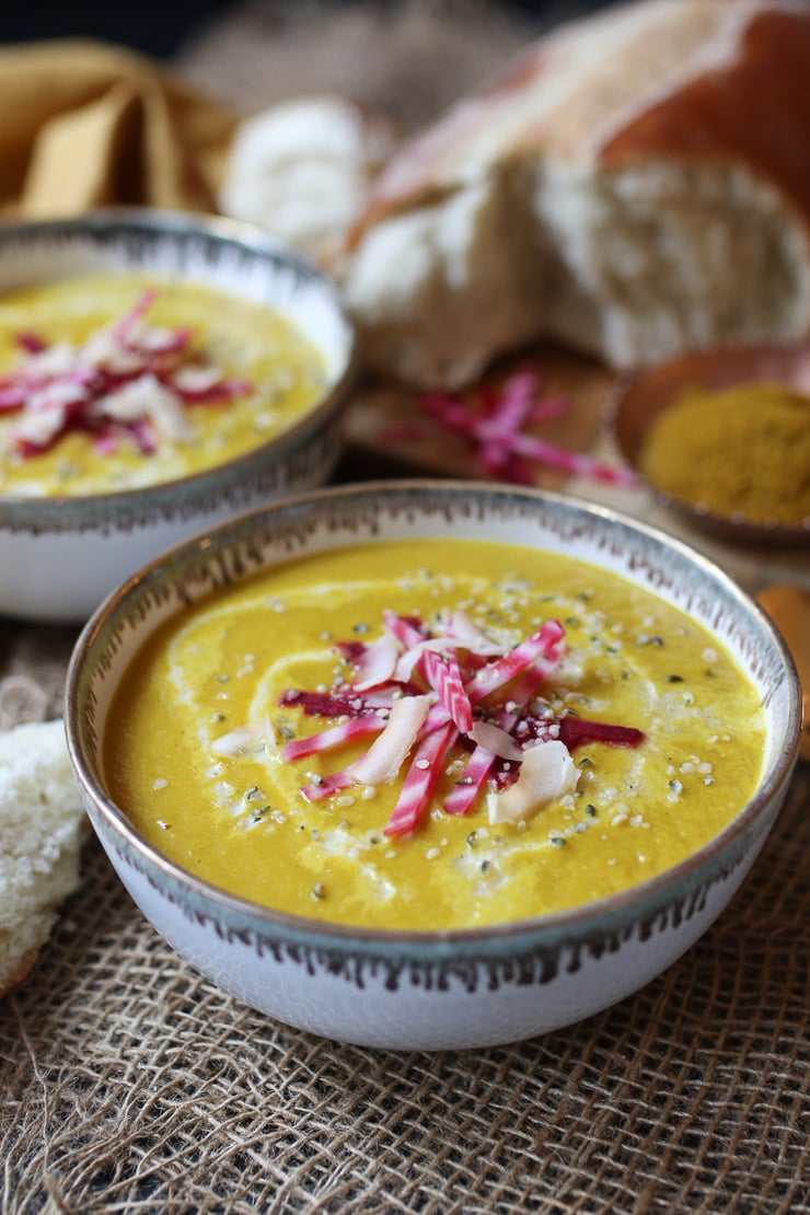 yellow vegan soup recipe in a white bowl topped with beets