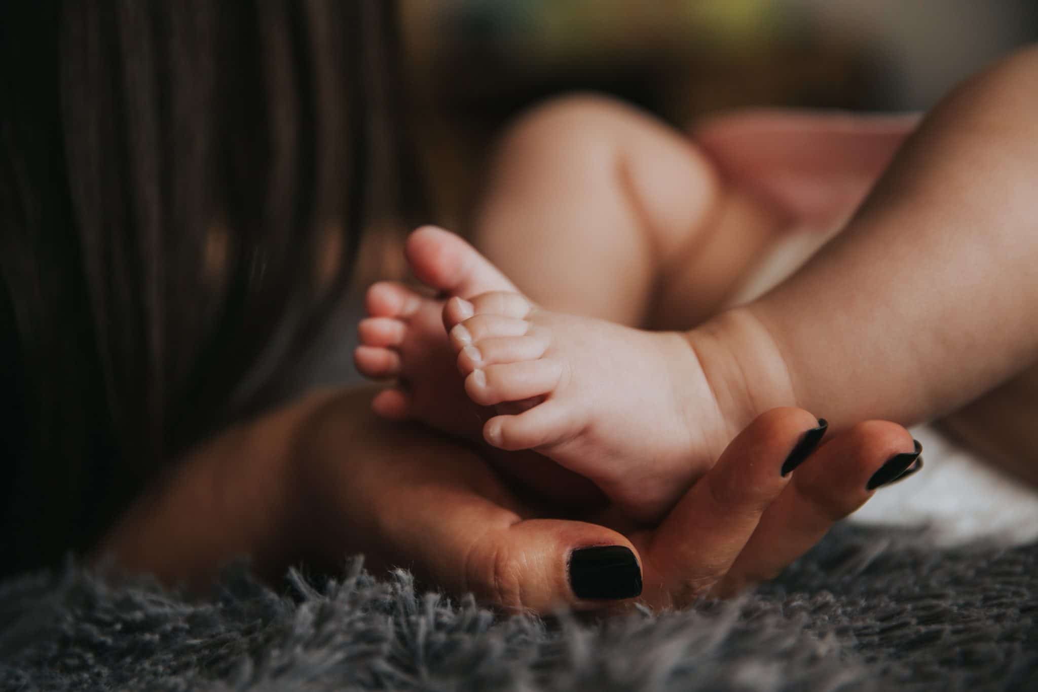 baby feet being held by a womans hand with black nail polish