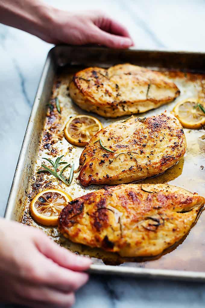 full shot of baked lemon chicken on a sheet pan garnished with fresh herbs