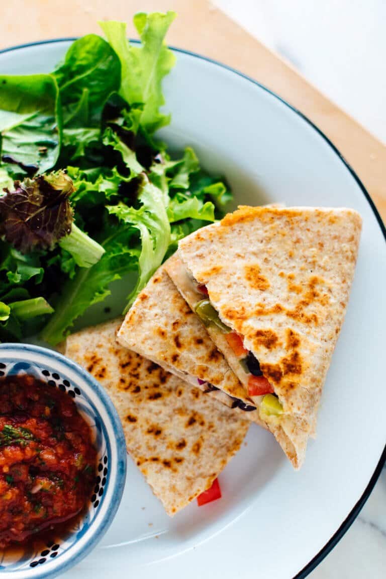 birds eye view of quick pantry staple quesadilla recipe served with greens and a small bowl containing salsa on a white plate