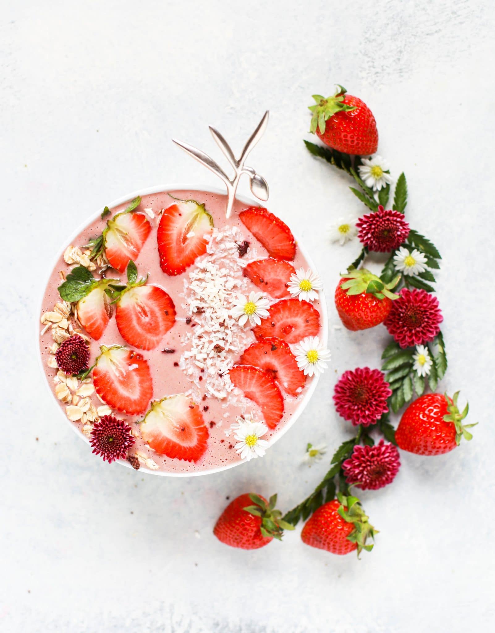 birds eye view of a vegan strawberry smoothie bowl against a white background with additional fresh strawberries lying next to the bowl