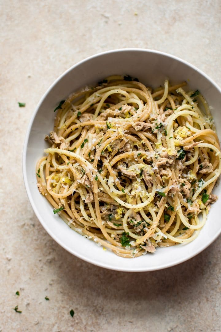 birds eye view of easy pantry staple canned tuna pasta served in a white bowl garnished with fresh herbs and cheese