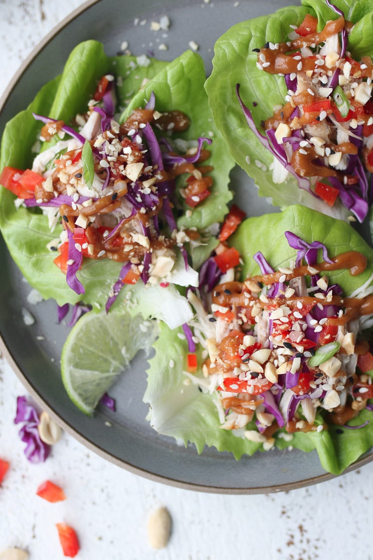 Birds eye view of three healthy chicken lettuce wraps on a grey plate topped with veggies, and peanut sauce 