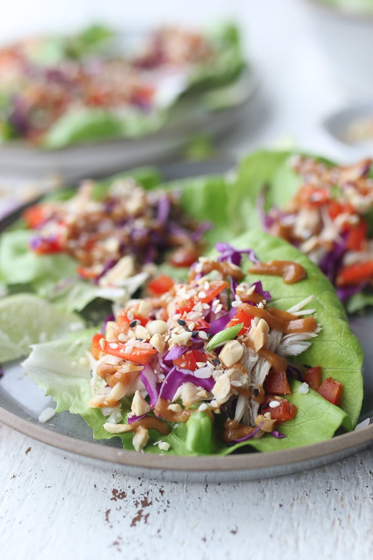 Three healthy chicken lettuce wraps on a grey plate topped with green onion 