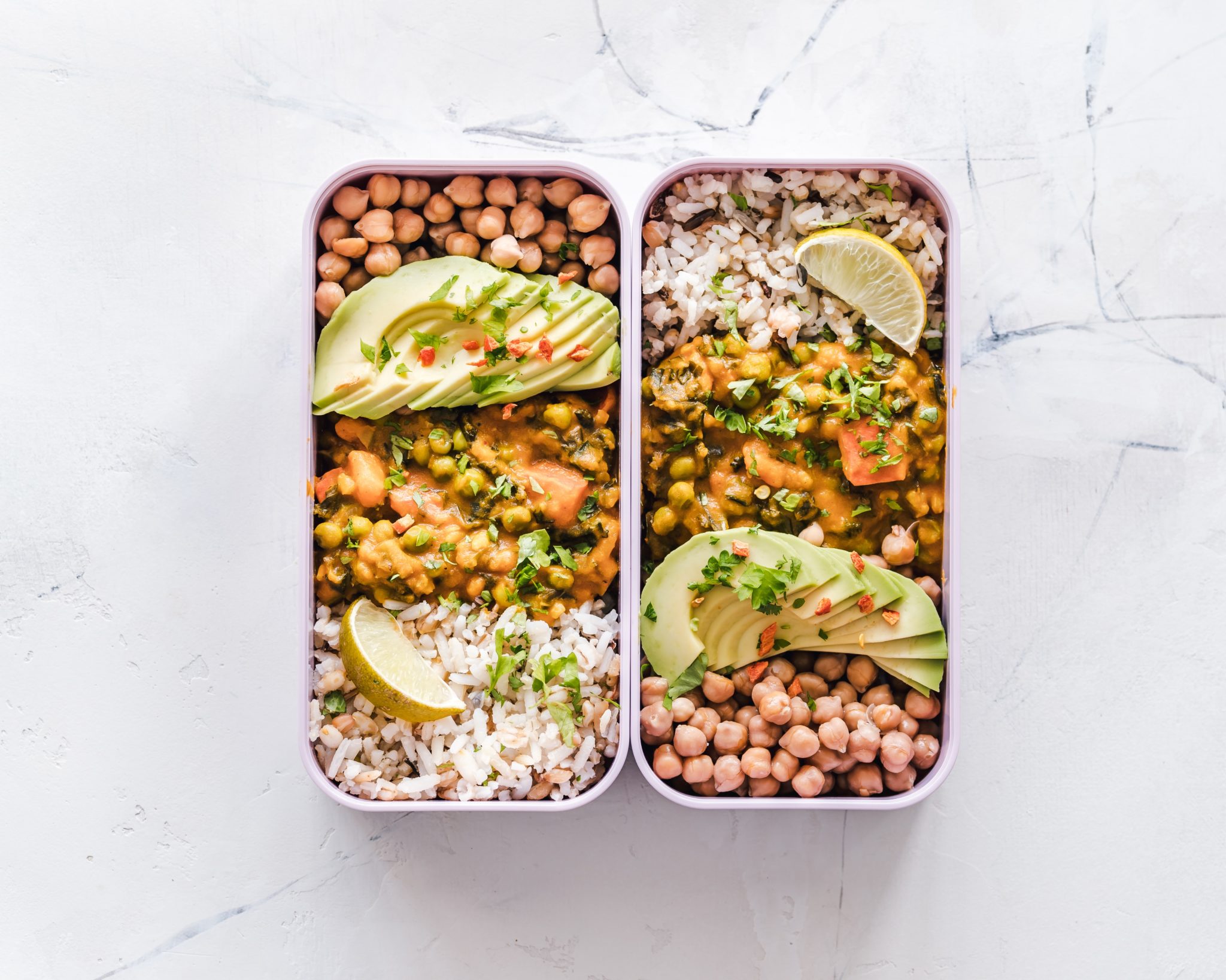 birds eye view of healthy meal prepped food in rectangular containers against a marble background