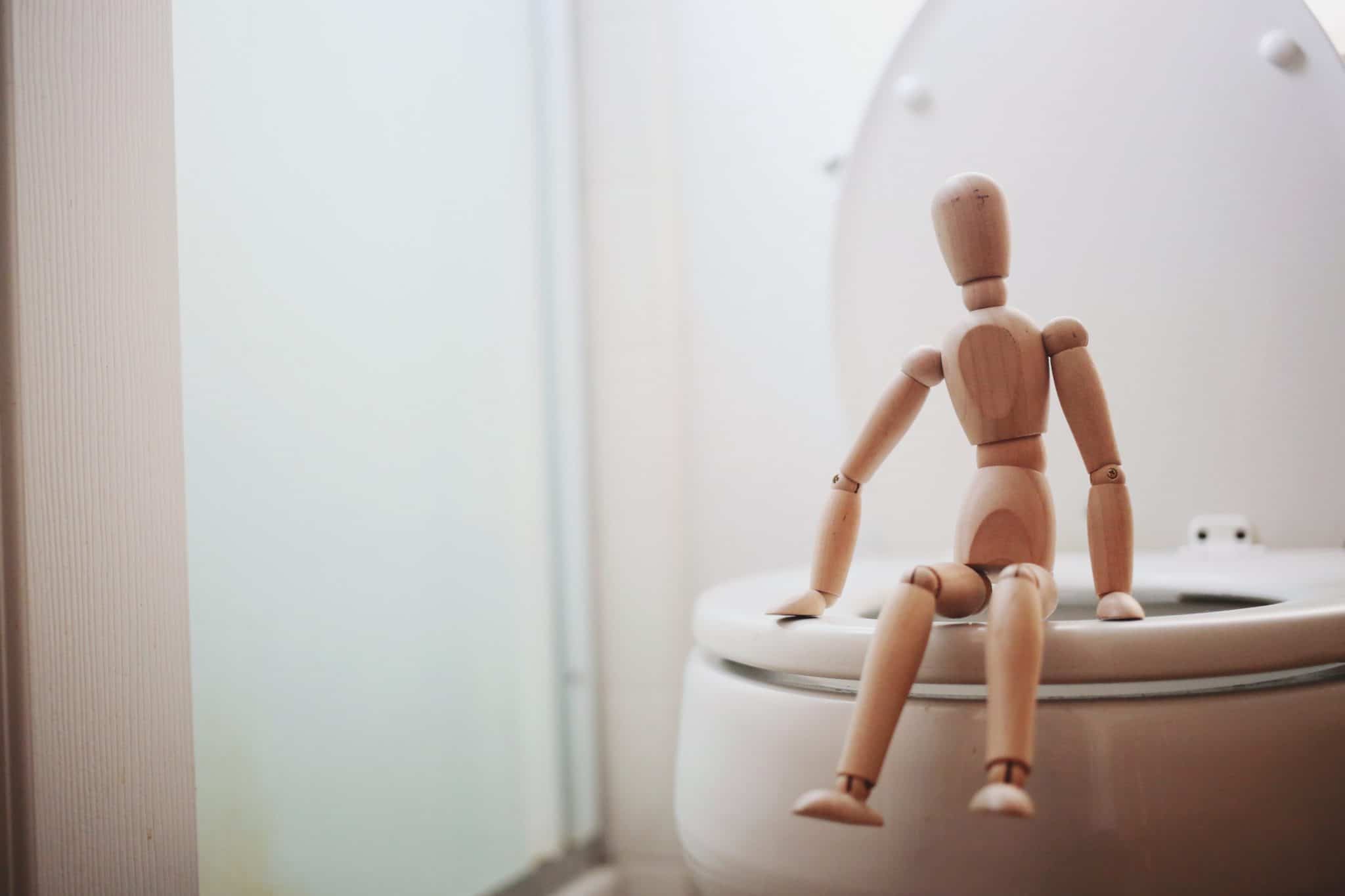 close up of a wooden action figure sitting on the toilet