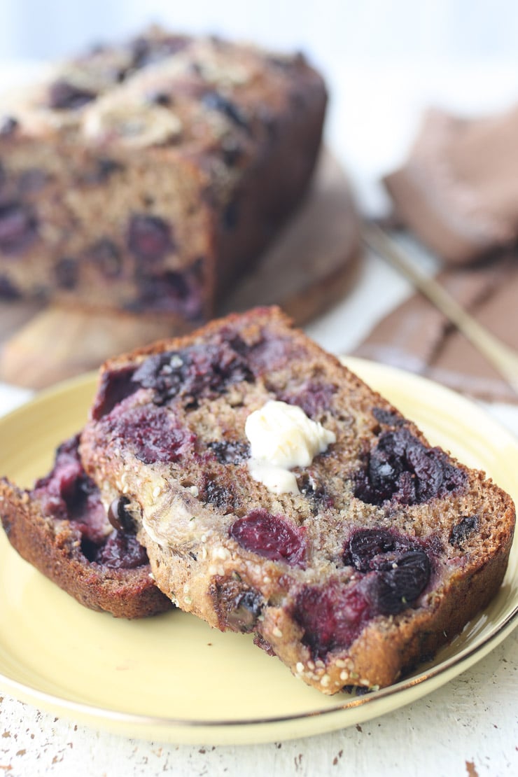 Two slices of dairy free banana bread on a yellow plate topped with butter with remainder of loaf on a wooden plate in the background.