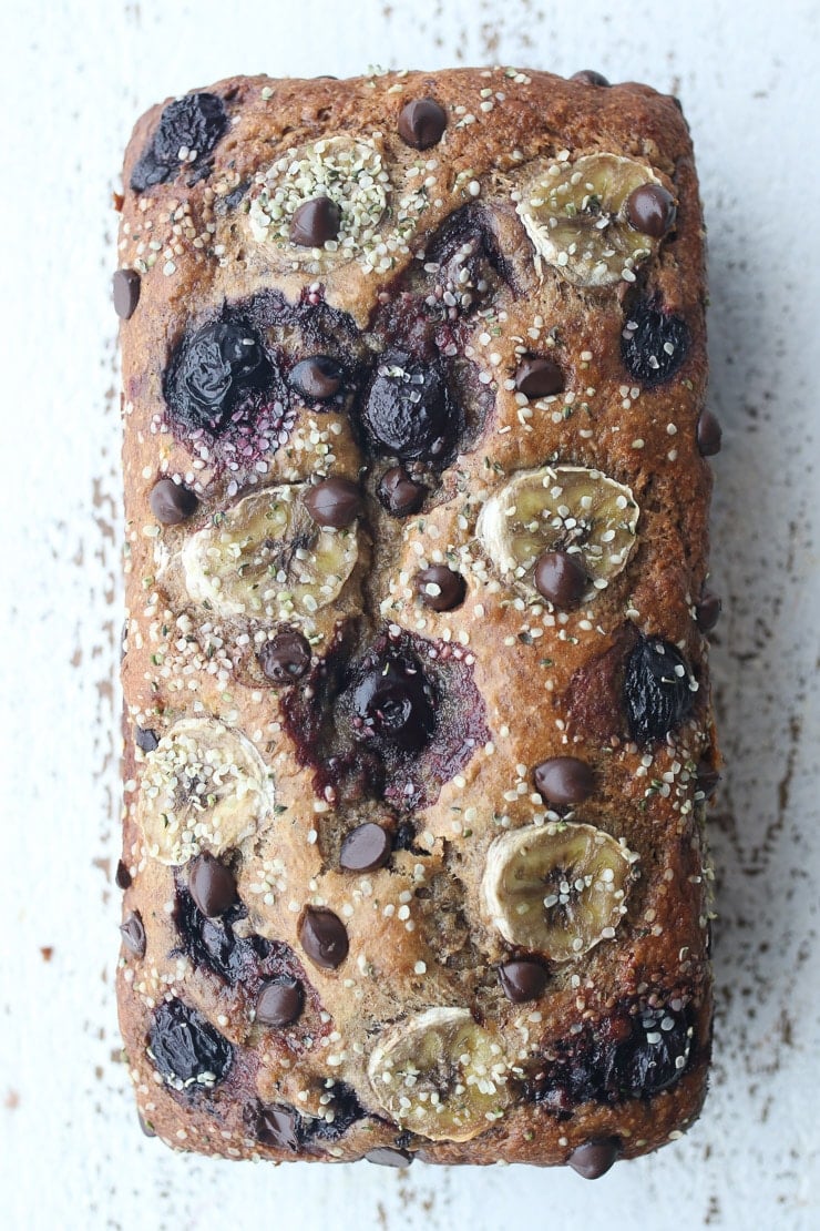 Birds eye view of banana bread loaf with banana coins, chocolate chips, cherries, and hemp seeds.