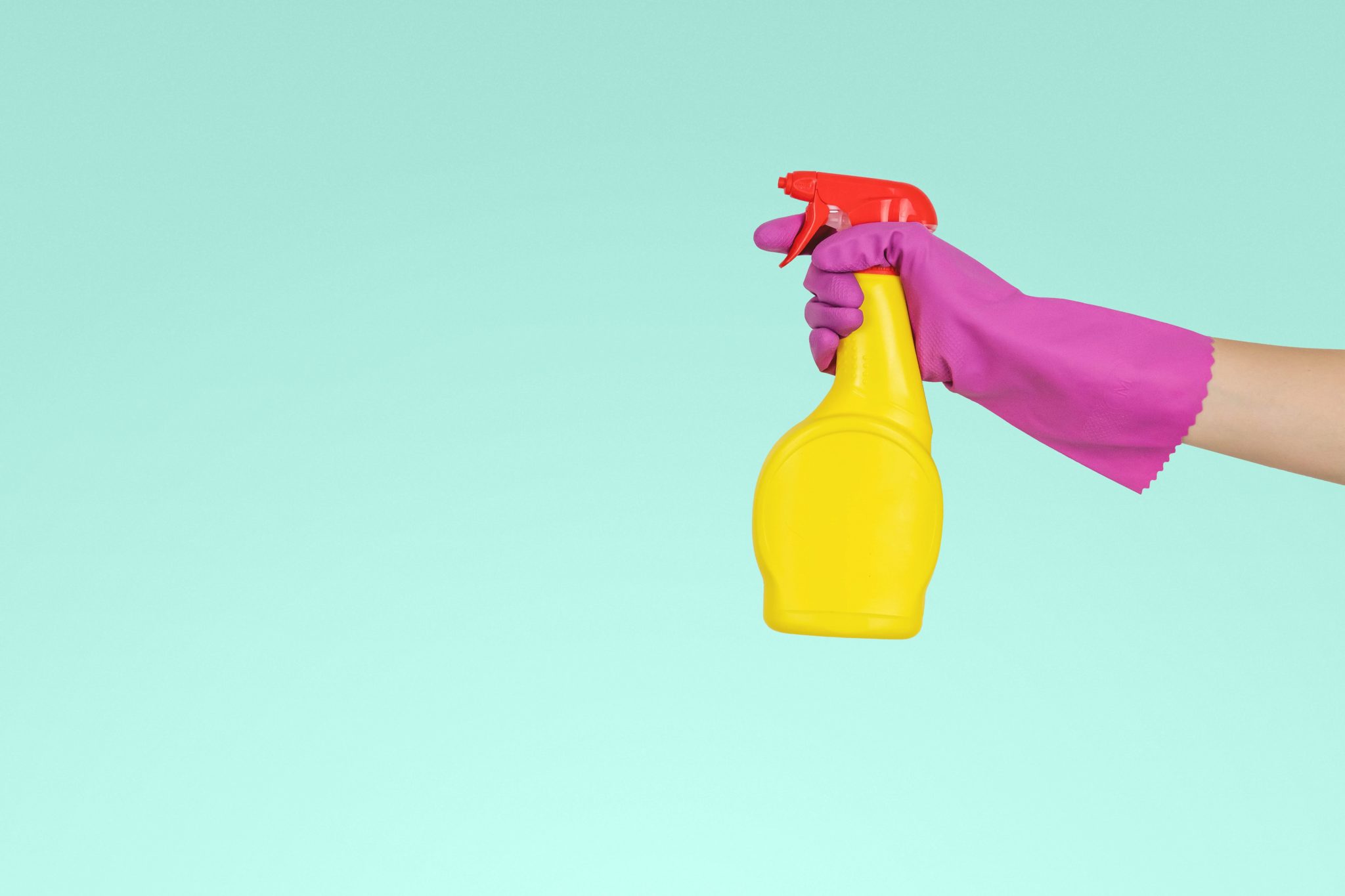 image of a pink dish glove holding a yellow disinfectant bottle for COVID-19 against a light blue background