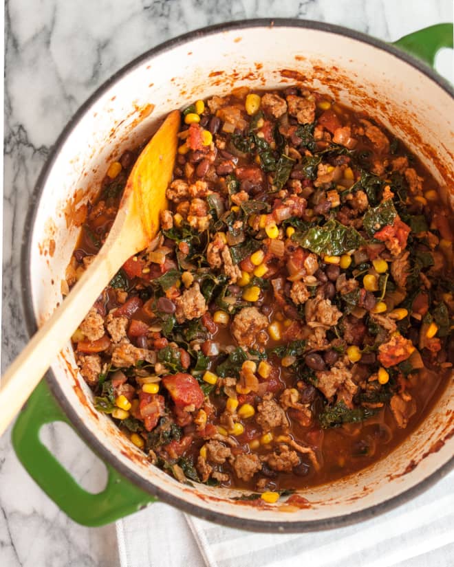 birds eye view of a large green pot filled with easy turkey and kale chilli with a wooden stirring spoon 