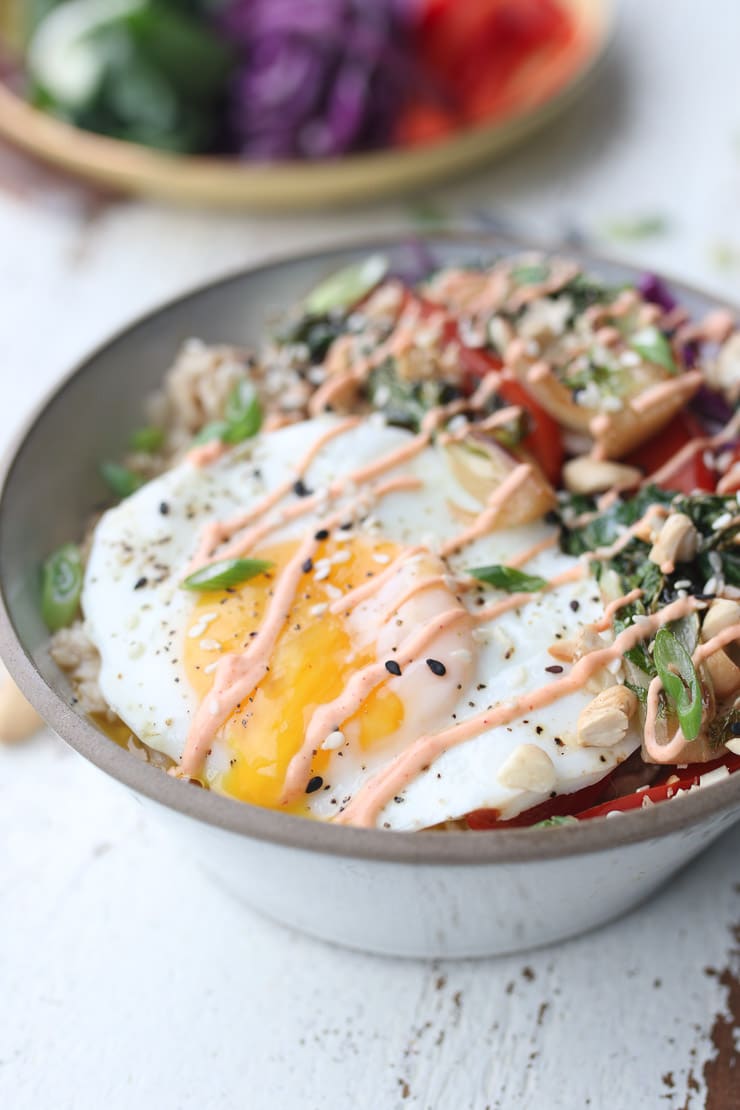 close up of a runny egg inside of a savoury korean oatmeal bowl garnished with onions, sesame seeds, and spicy sauce