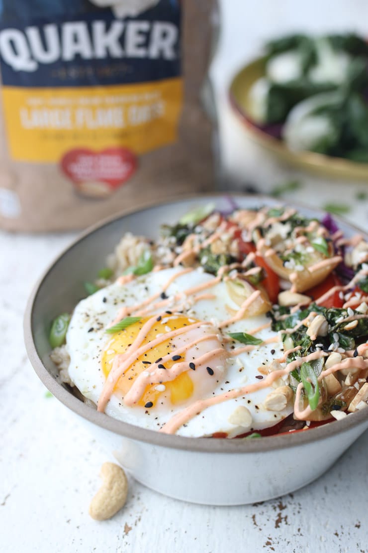 full shot image korean spiced savoury oatmeal bowl topped with spicy sauce, green onions, and sesame seeds in a grey bowl with a package of quaker oats in the background