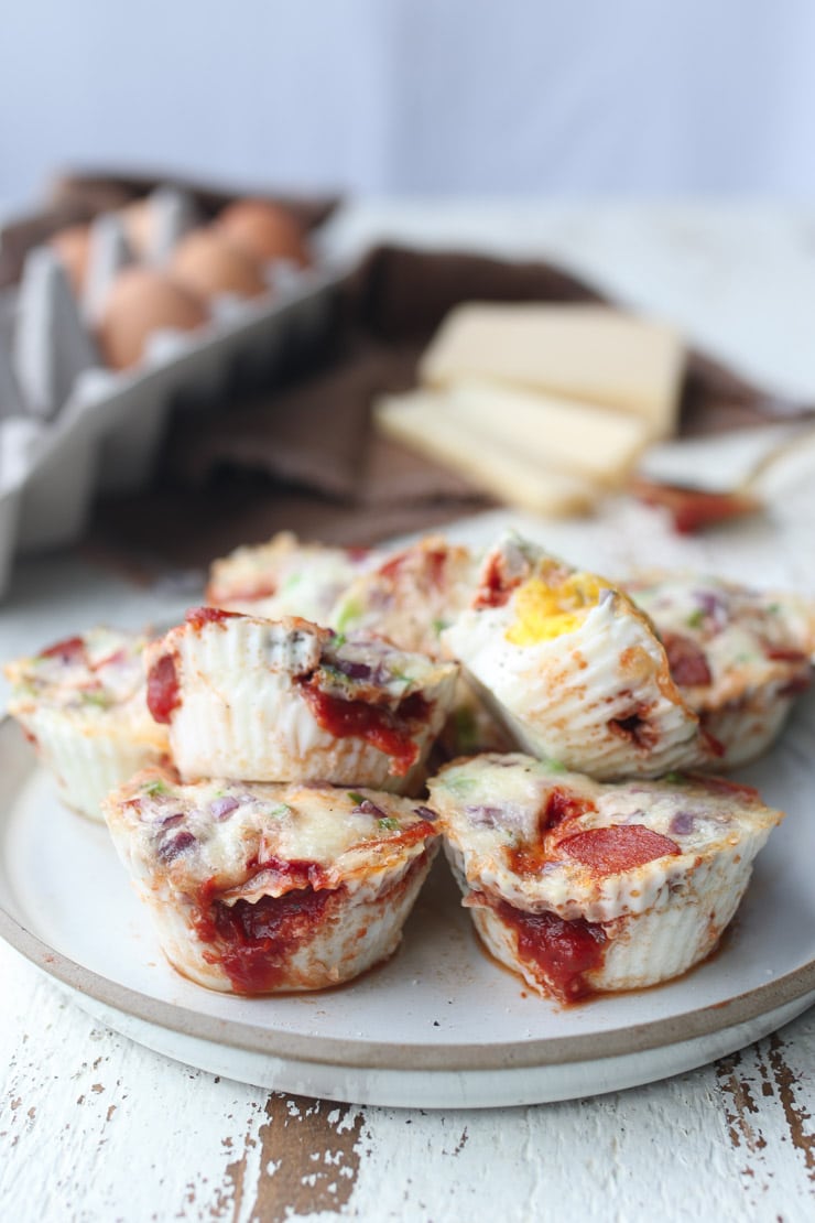 multiple keto and gluten free egg breakfast muffins stacked on top of each other on a white plate with a carton of eggs in the background