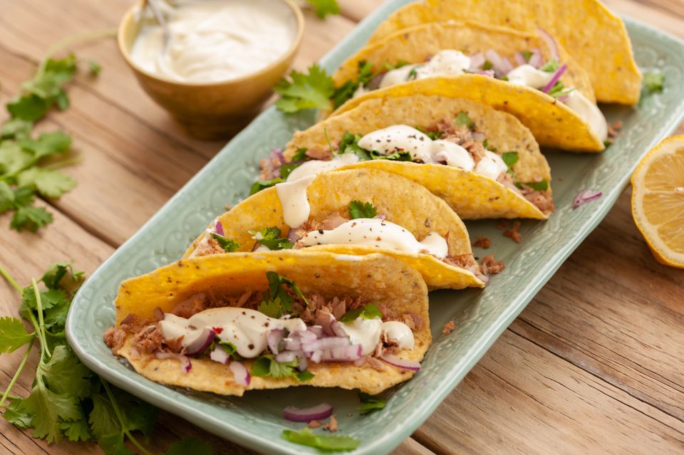 full shot image of five canned tuna fish tacos on a rectangular green plate garnished with fresh herbs and aioli