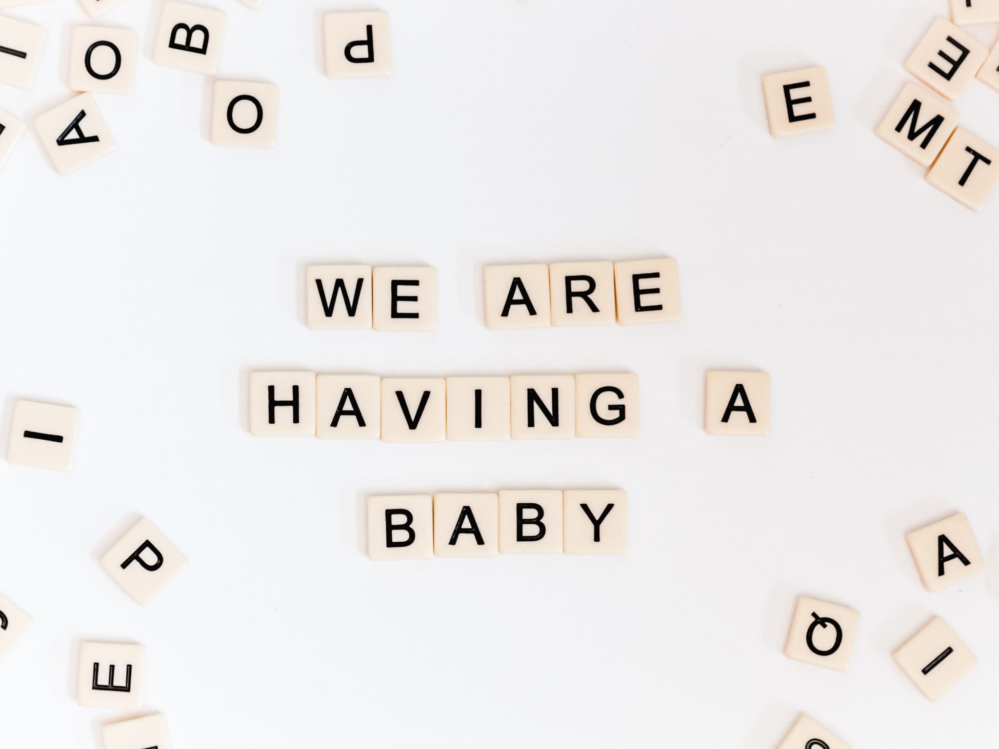 image of beige tiles spelling "we are having a baby" on a white background