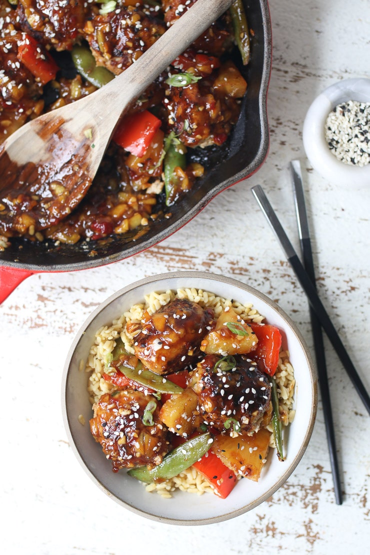 Hawaiian chicken meatballs on a white plate with chopsticks, sesame seed, and pot in the background. 