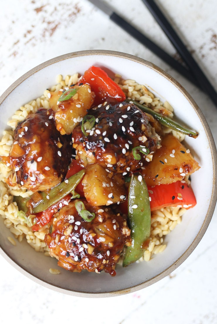 Hawaiian meatballs in white plate on top of a bed of rice topped with sesame seeds 