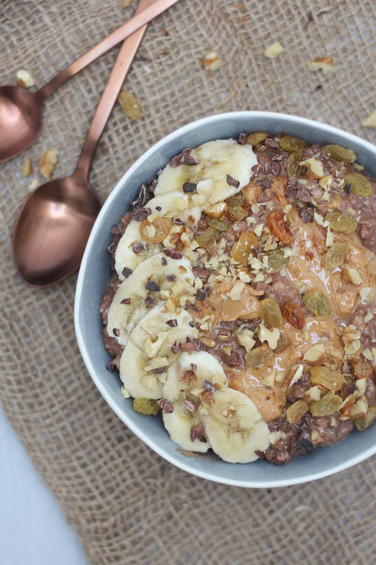 birds eye view of chocolate zucchini oatmeal in a blue bowl garnished with fresh and dried fruit with a rose gold spoon