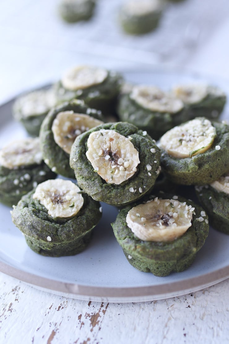 group of egg and gluten free green mini muffins for toddlers on a large white plate garnished with hemp hearts and banana slices