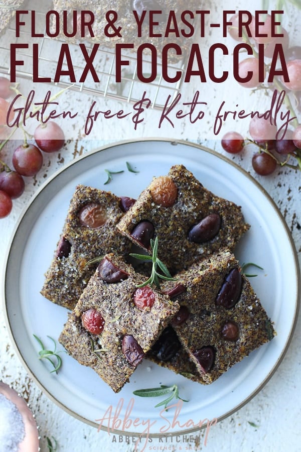 pinterest image of flour and yeast free flax focaccia bread topped with olives and fresh herbs on a white dish and a side of red grapes with text overlay