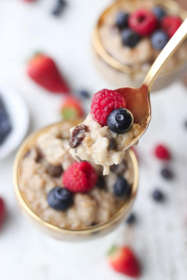 close up of vegan oatmeal pudding on a gold spoon topped with berries and raisins 