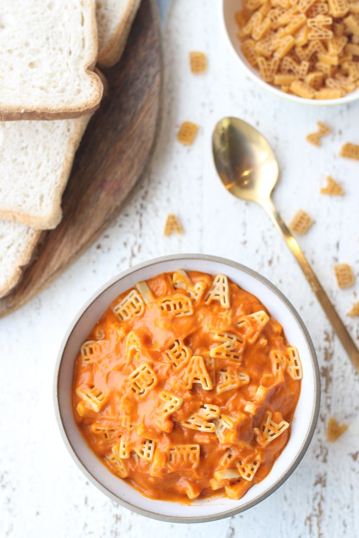 birds eye view of a white bowl containing vegan alphagetti with hidden veggies and pantry staples next to a gold spoon and slices of toast