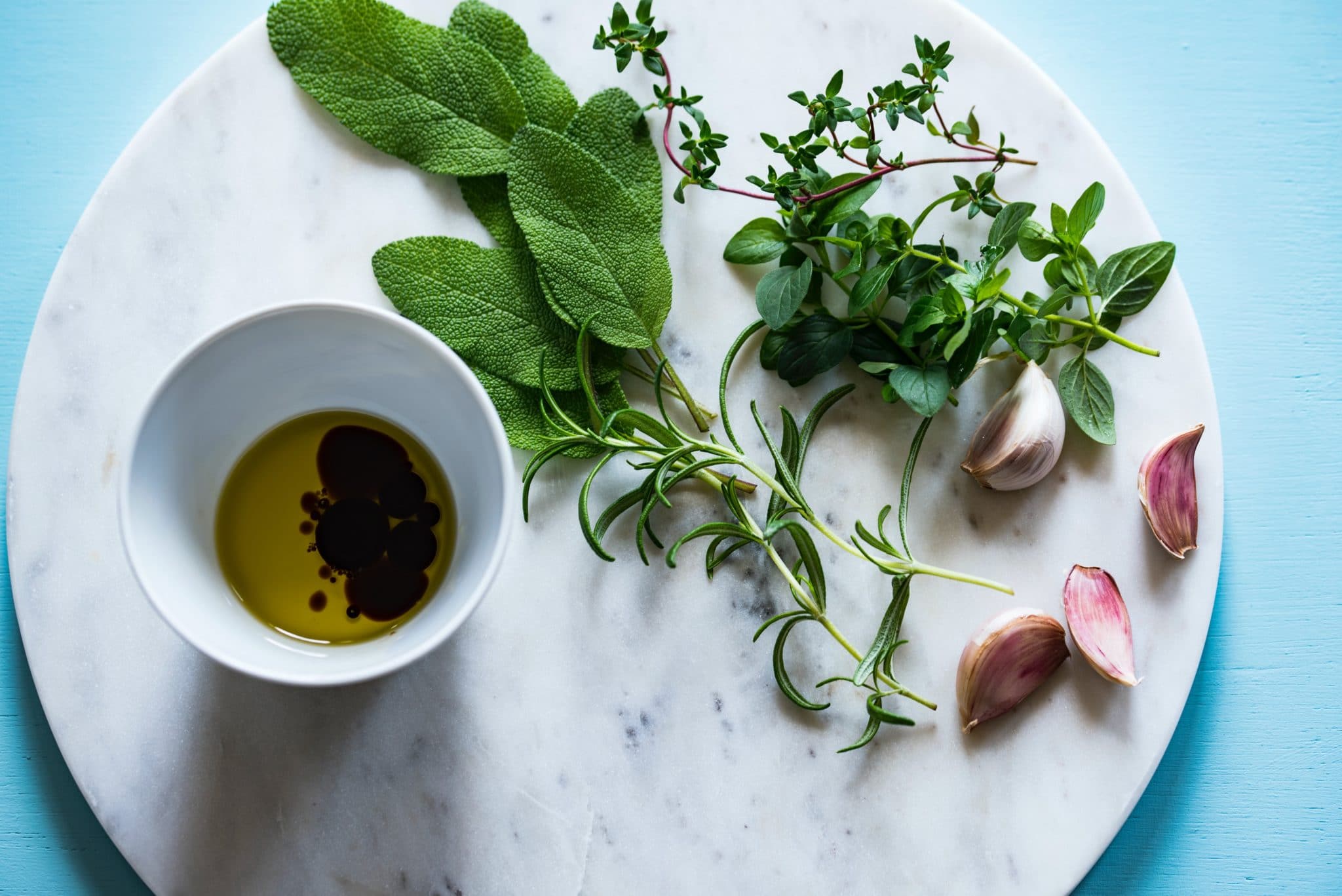 birds eye view of oil and vinegar in a white bowl with a variety of herbs laid out on a plate 