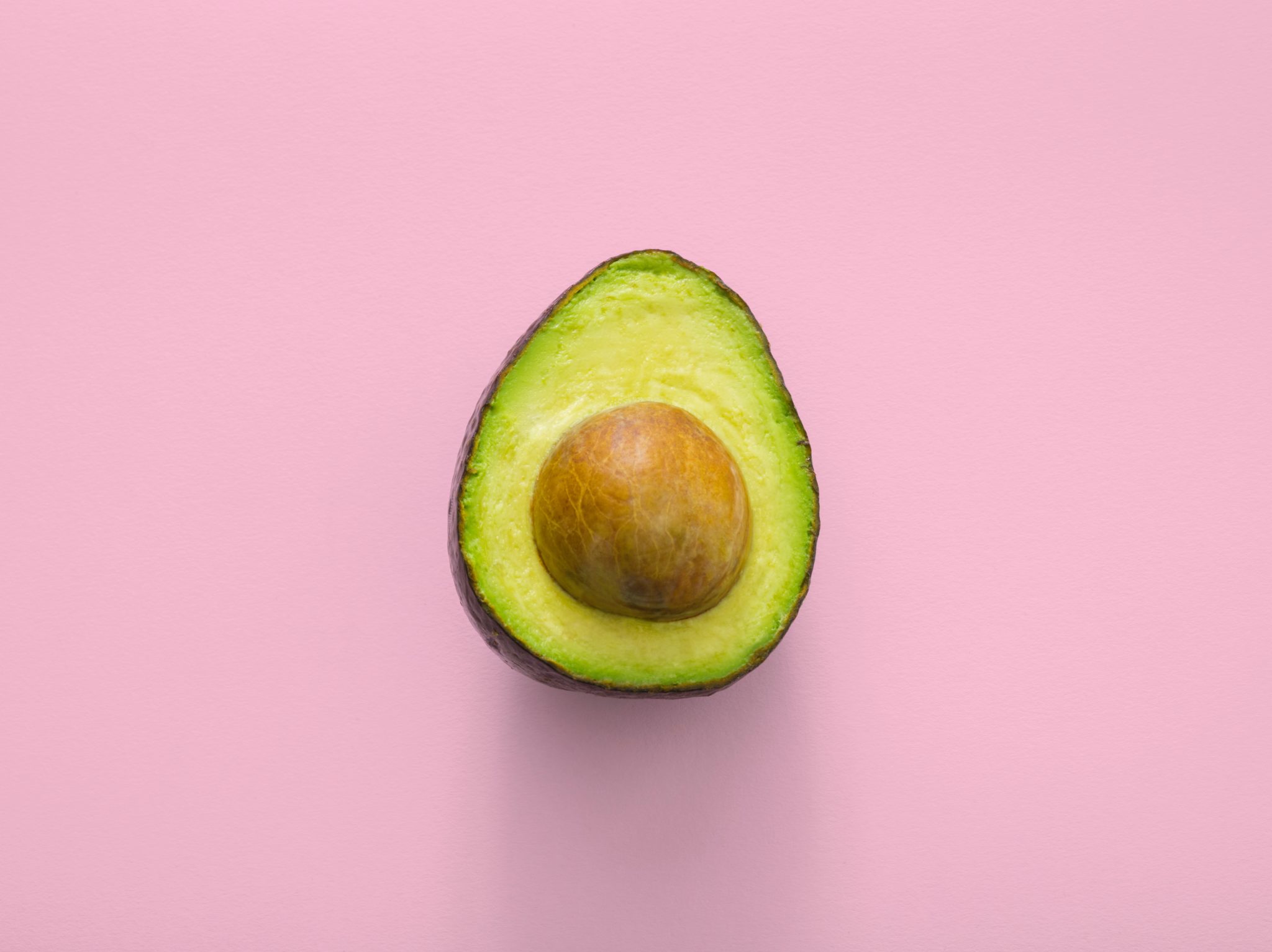 close up of half of a ripe avocado against a light pink background