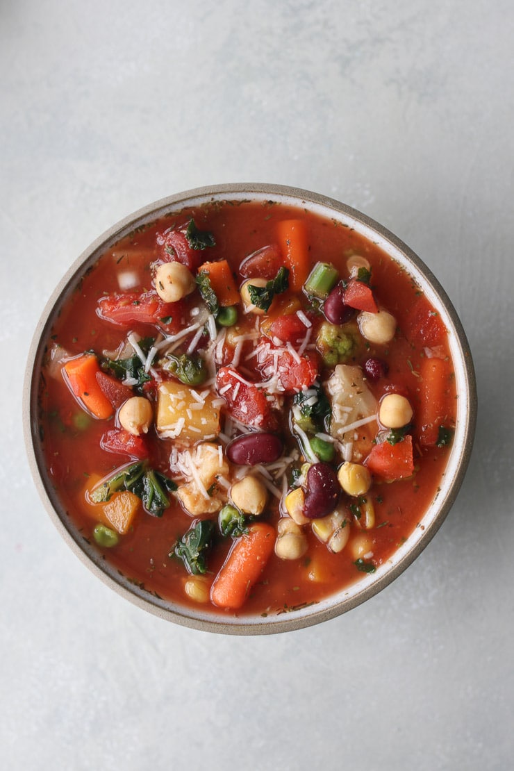 birds eye view of vegan bean and frozen vegetable soup in a white bowl garnished with vegan cheese