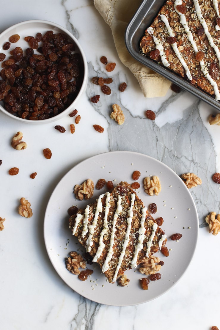 Birds eye view of baked oatmeal recipe topped with walnuts and raisons with a bowl of raisins and sheet pan in the background.