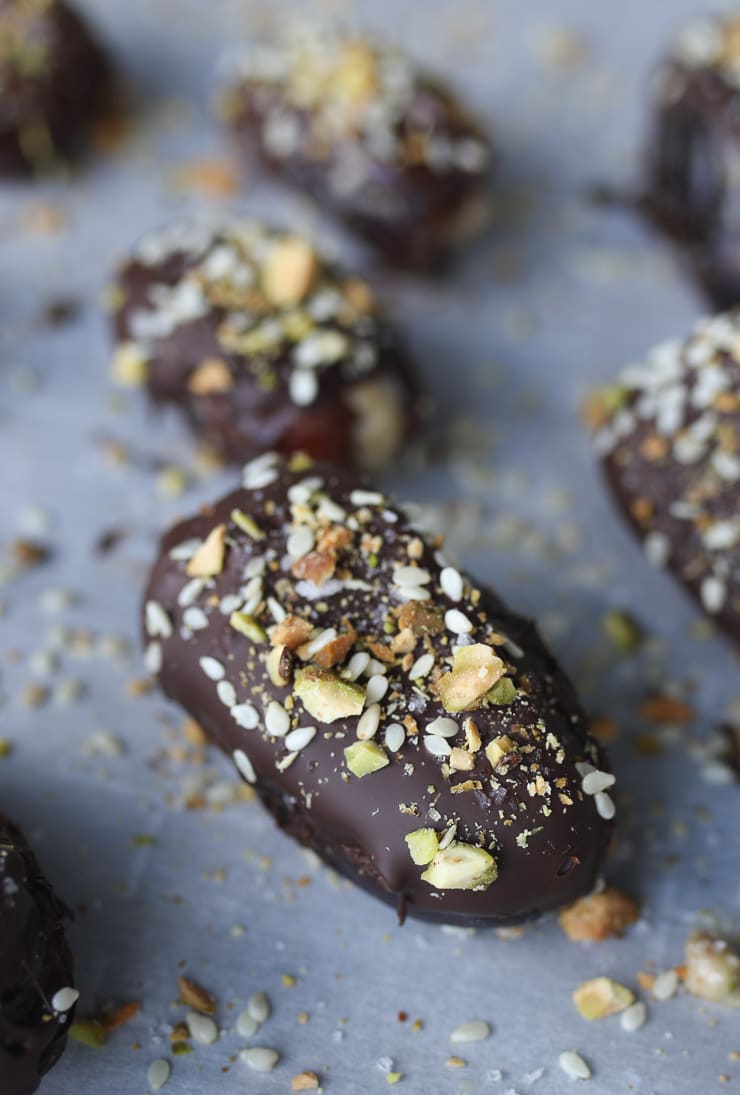 Chocolate covered dates on a baking sheet topped with pistachios.