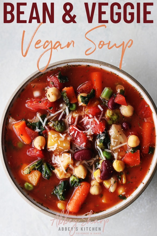 pinterest image of vegan soup made with beans and vegetables in a white bowl topped with vegan cheese with text overlay