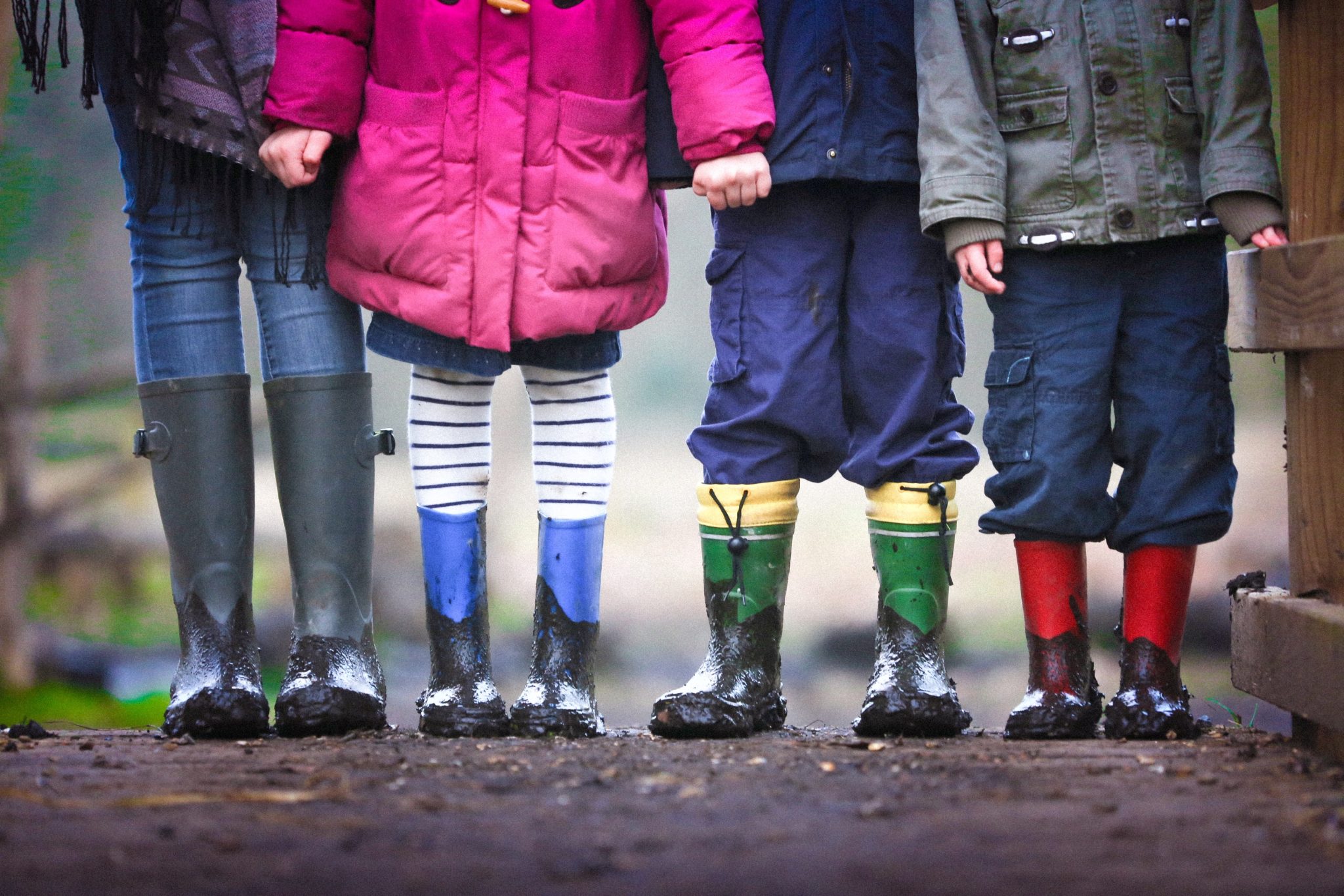 Four children who take probiotics wearing rain boots standing side by side holding hands.