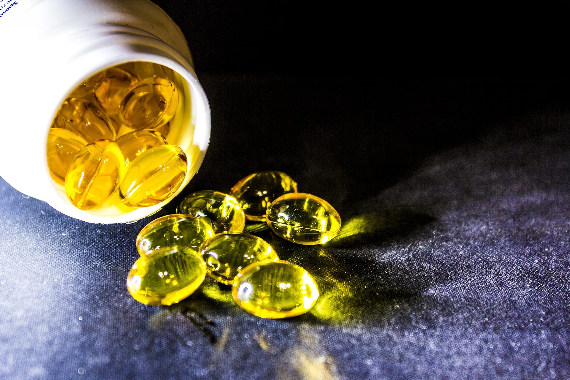 close up of translucent yellow fertility supplements coming out of a white pill bottle against a dark background