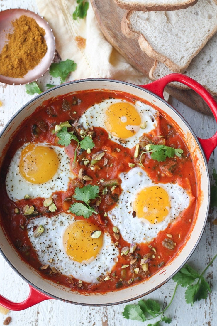 birds eye view of curry shakshuka in a red pot garnished with parsley and pistachios 