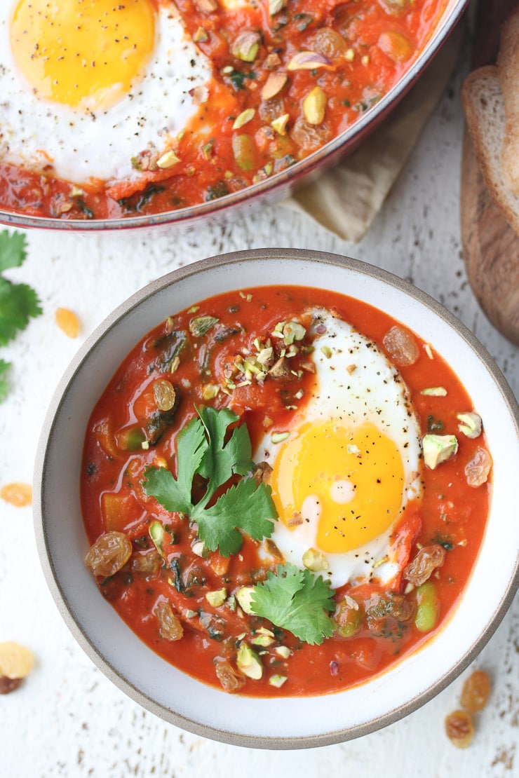 birds eye view of curry flavoured egg shakshuka garnished with fresh herbs served in a large white bowl.