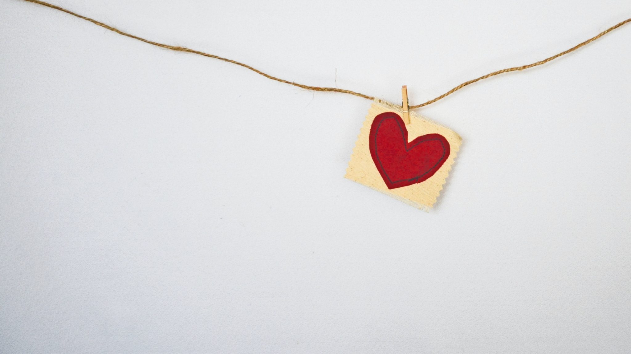 close up image of a red heart painting on a square canvas hanging from a rope against a white background