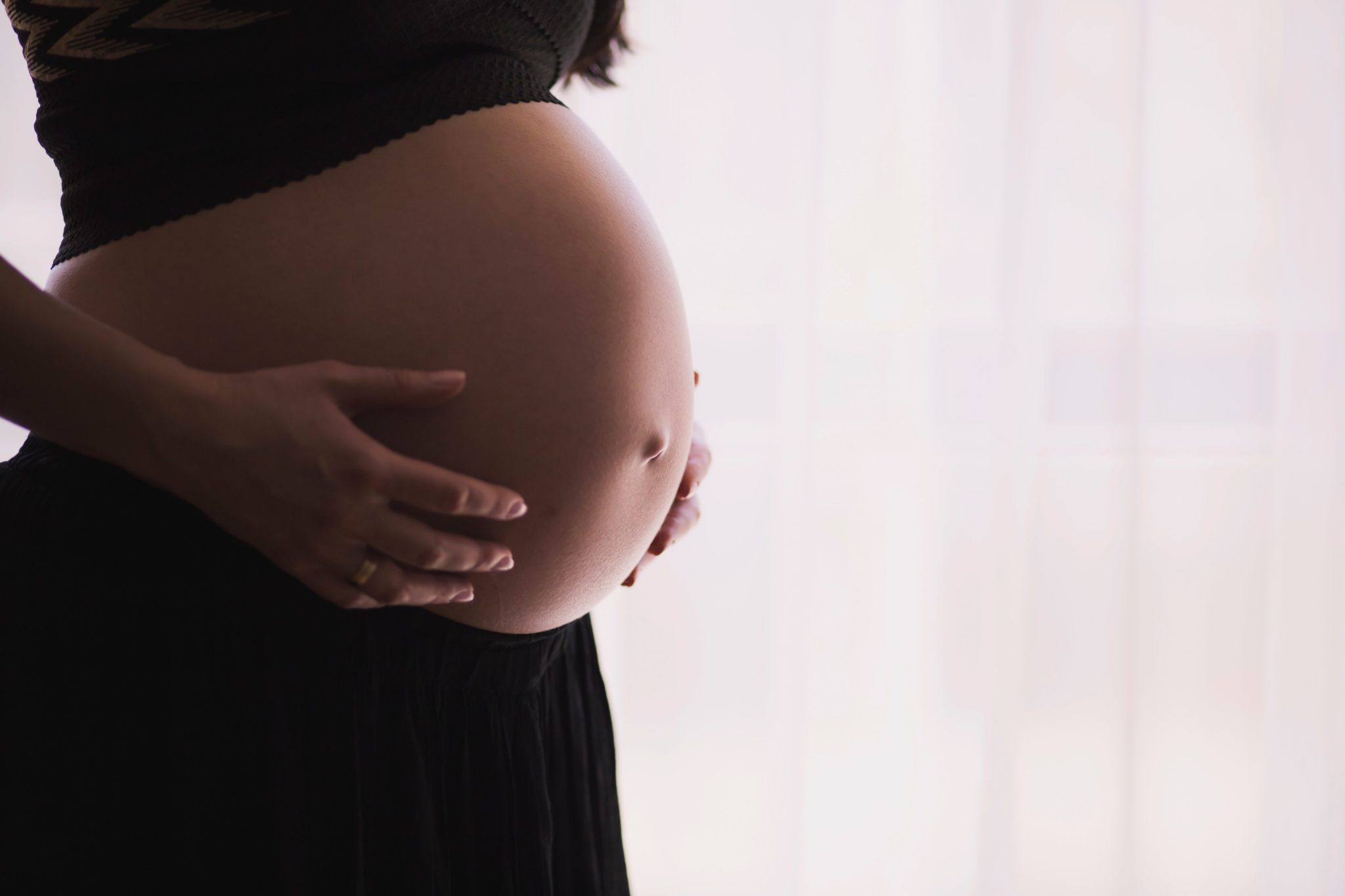 image of woman with visible pregnant stomach holding her stomach standing sideways