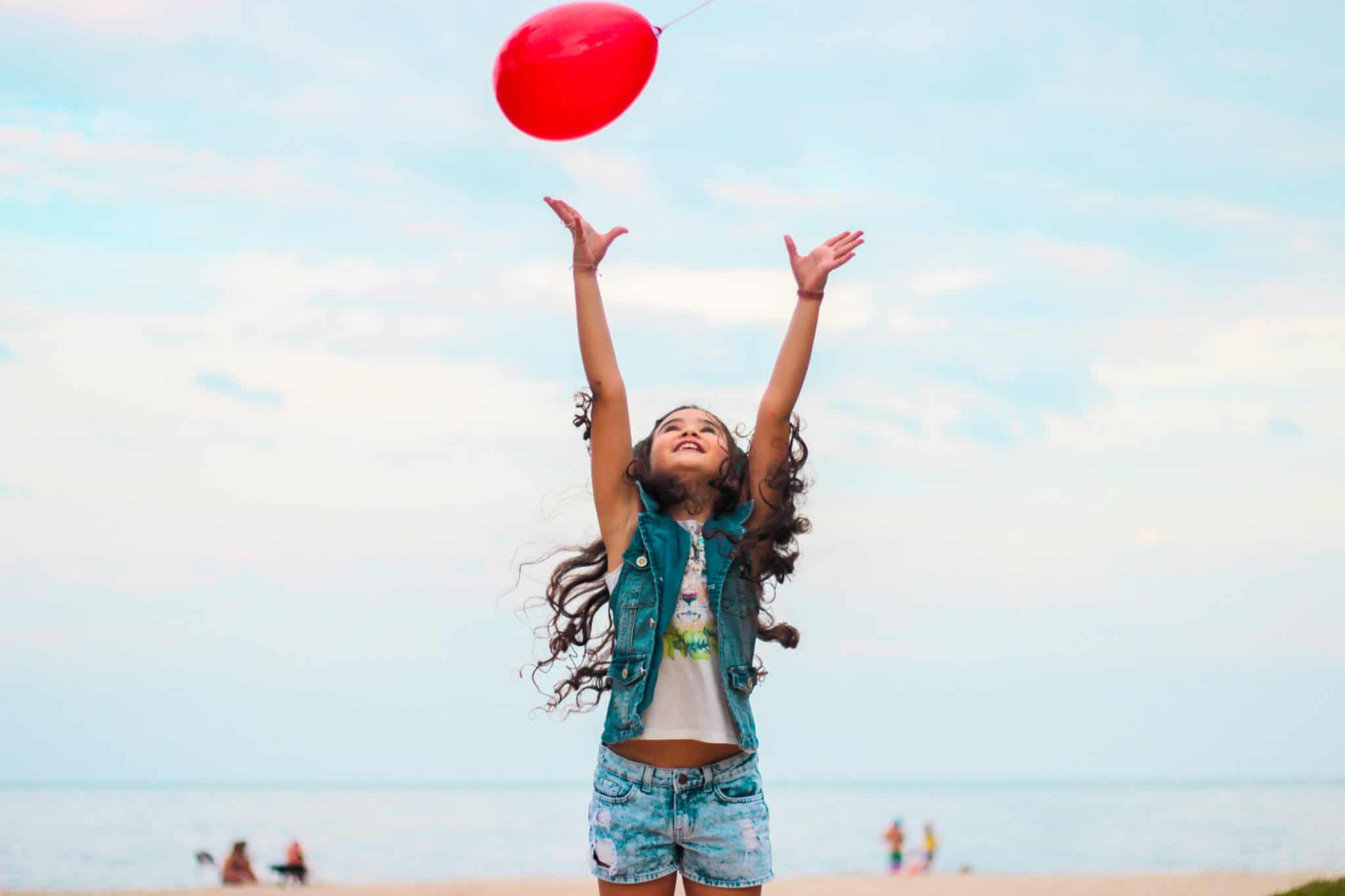 Little girl on the beach playing with a balloon.