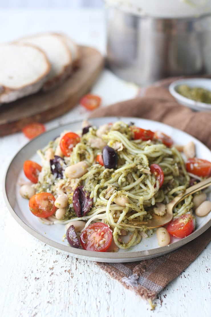 Close up of tuna pasta recipe with pesto sauce on a white plate with fresh bread in the background.