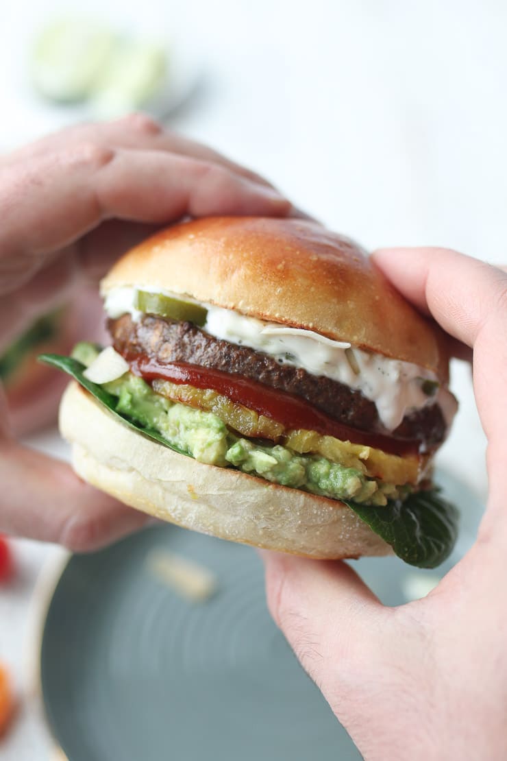 two hands holding veggie burger with pineapple, guac, and lime aioli 