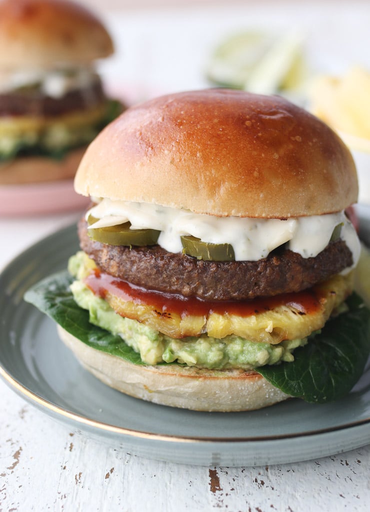 full shot image of hawaiian spiced vegetarian burger with avocado, pineapple, and homemade lime aioli on a grey plate